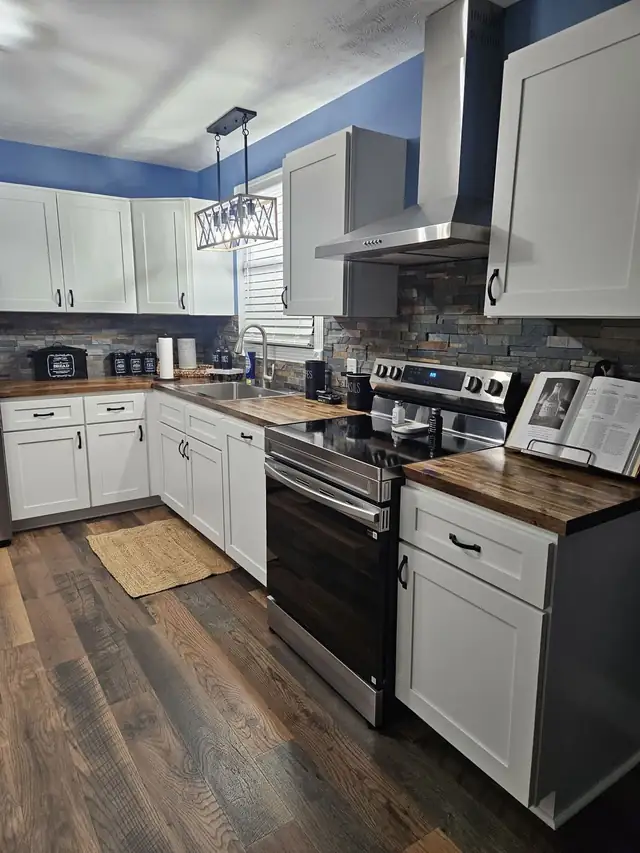Kitchen with white shaker cabinets, wood-tone countertops, stacked stone backsplash, stainless range hood and plank flooring