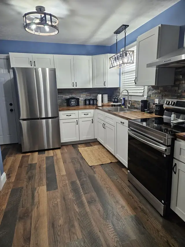 Kitchen remodeled by Matt's crew, with white cabinets, stainless refrigerator, wood-tone counters and plank floor