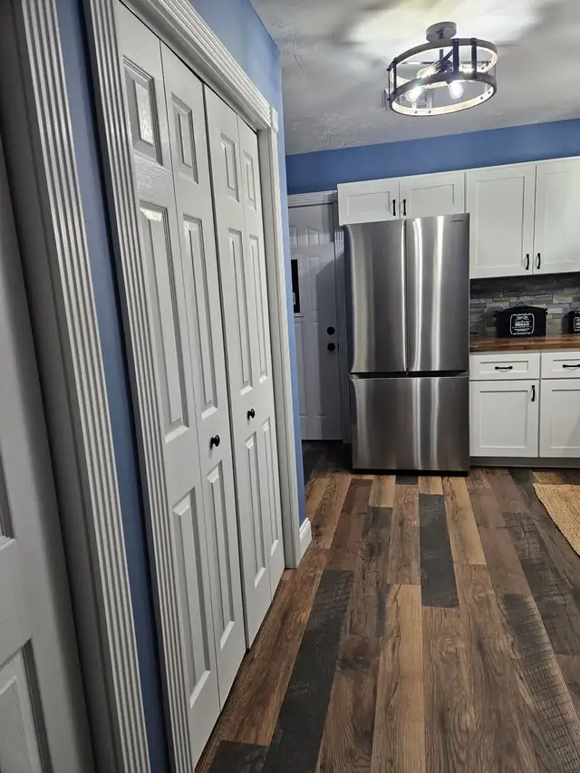 Kitchen with white cabinets, a stainless refrigerator and wood-look plank flooring beside white closet doors